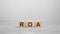 three wooden blocks with the letters ROA on the gray table. business concept