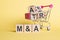 Three wooden cubes with letters - M and A, on yellow table, space for text. M and A - short for Mergers and Acquisitions