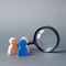 Three wooden human figure stands near a magnifying glass on a gray background. Search for vacancies and work. Human resources