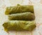 Three wrapped pieces of meat in green vine leaves a decorated board