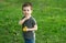 Three year old caucasian toddler boy holds a yellow dandelion in his hands.