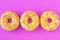 Three yellow round donuts with a hole on a pink background. Top view. Funny mood concept. Laconic food design.
