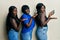 Three young african american friends using smartphone pointing aside with hands open palms showing copy space, presenting