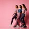 Three young athletic girls in high-tech modern colorful sportswear vigorously walk together towards free text space on pink