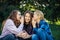 Three young attractive woman sharing secrets sitting on green grass in the park. Cheerful girlfriends gossip and whisper outdoor