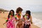 three young and beautiful latin women with a glass of blue cocktail stroll along the beach happily talking to each other and