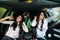 Three young beauty girls driving in a car dancing and having fun in city street