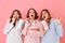 Three young girls 20s wearing colorful striped pyjamas expressing excitement or thrill while watching movie at slumber party and