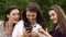 Three young girls looking on phone, smiling on nature. Slowly