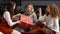 Three young girls sitting on the couch and having fun unwrapping Christmas presents at home