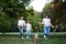 Three young girls, wearing blue jeans and white shirts, running in green park with small dog in summer. Family fun walk with