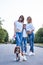 Three young girls, wearing blue jeans and white t-shirts, walking with small dog in city park in summer. Family fun leisure time