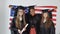 Three young happy graduate women of different nationalities stand together side by side and hold diplomas and USA flag