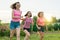 Three young sports girls teenagers running on a green lawn against the backdrop of summer sunset