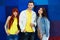 Three young stylish friends standing close on bright background