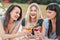 Three young women in blue dresses, and hats lie on plaid and drink wine. Outdoor picnic on grass on beach. Delicious