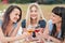 Three young women in blue dresses, and hats lie on plaid and drink wine. Outdoor picnic on grass on beach. Delicious