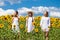 Three young women in white dress posing against the blue sky in sunflowers field