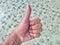 Thumb hand sign on blurred tile green background, agree thumb sign, hand up okay symbol, thumb up for agreement or ok gesture sign