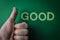 Thumb up beside the word Good written with plastic letters on green paper background