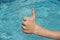 thumbs up sign of young man, teenager with blue water as background