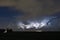 A thunderstorm with a clearly visible anvil is illuminated by lightning