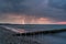 Thunderstorm with flashes striking in the ocean captured at the beach right after sunset with groynes in the for