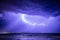 Thunderstorm with lightning at dramatic sky over sea on coast with mountains in the background