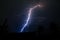 Thunderstorm strikes through the sky making bright light. Silhouette of homes and trees underneath