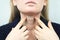 Thyroid gland. Closeup portrait of cute sick young blonde woman in white top having sore throat, holding hand on her neck