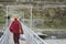 Tibetan monk, with back to the camera, holding groceries in a plastic bag, crossing a bridge