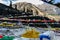 Tibetan prayer flags waving and swaddled with trees an mountain in sideway over frozen river with mountain in background.