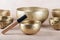 Tibetan singing bowls with sticks used during mantra meditations on beige stone background, close up