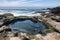 tidal pool surrounded by cliffside rocks, with view of the open ocean