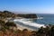 The tide rolls in to the shore around a bay and headland south of Mendicino California with defocused purple flowers in the foregr