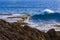 Tidepool on ledge above ocean, water cascading. Wave with white crest; blue sea beyond.