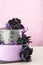 Tiered wedding cake with black fake flowers on pink background