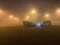 Tight fog on the large parking illuminated by multiple lights and three parked cars