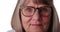 Tight shot of somber elderly woman wearing eye glasses on white background