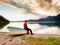 Tiired man in red shirt sit on old fishing paddle boat at mountains lake coast.