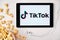 TikToK logo on the screen of the tablet with popcorn box and Apple earphones on the background. Application for creation