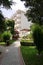 A tiled walkway running between green lawns to a gazebo for rest and a hotel