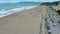 tilt aerial footage of Ocean Beach with people relaxing in the sand and surfing, blue ocean water, lush green trees and homes