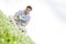 Tilt image of young man reading book while sitting on grass against sky