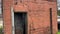 Tilt of an old overgrown red brick single jail unit open iron door with lock