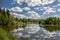 Tilt and shift view of sunny village river with clouds, tree, swamp and blue sky