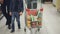 Tilt-up shot of happy young family pushing shopping trolley full of tasty food through supermarket. Child is having fun