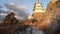Tilt up from snow covered path to reveal historic Japanese castle in golden light