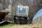 Tilted white intermediate bulk container or IBC plastic tank with metal cage put on top of wooden pallets in local garden to be