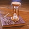 Time flow concept. Hourglass, old book and eyeglasses on wooden table, wooden background.Wooden hourglass counting time